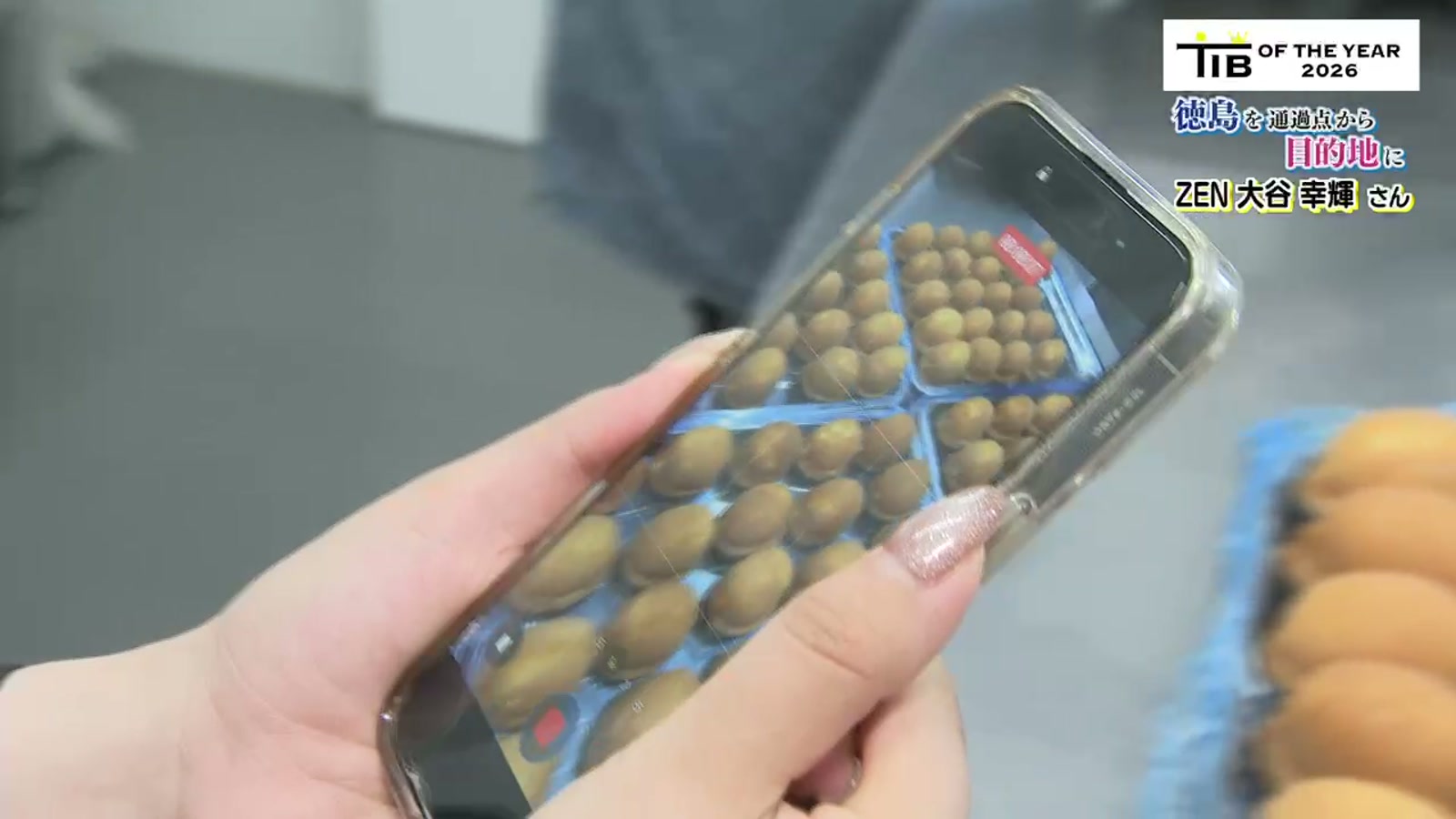 洋菓子店の商品を撮影した縦動画を、スマートフォンで確認する手元